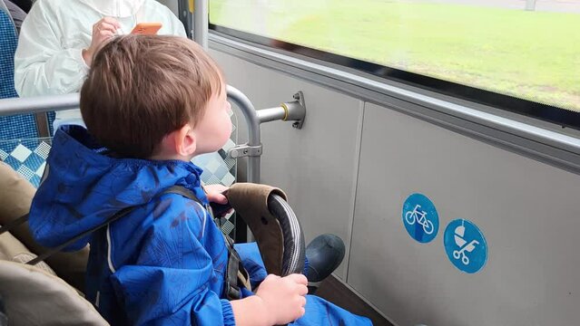 The child is sitting in a stroller on the bus, enjoying the open air and scenery outside. Kid boy aged two years (two-year-old)