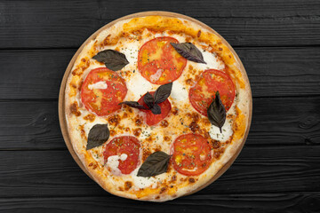 Pizza Margherita with tomatoes, basil and mozzarella cheese on black wooden background, close up. Top view