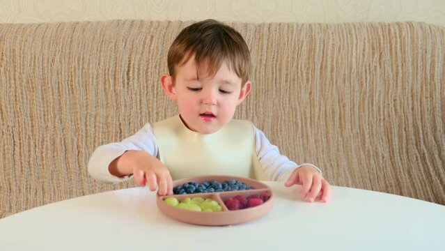 A mother woman gives her child a plate of fruits and berries