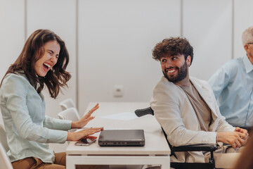 Disabled male person in wheelchair telling good news to his female colleague during brainstorming. Happy woman reacting to good news