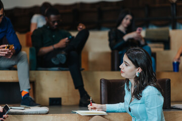 Brunette woman discussing project with teammate and writing information in a notebook
