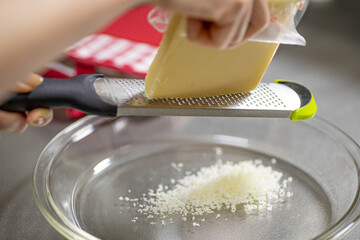 キッチンでチーズをグレーターで削る女性の手元