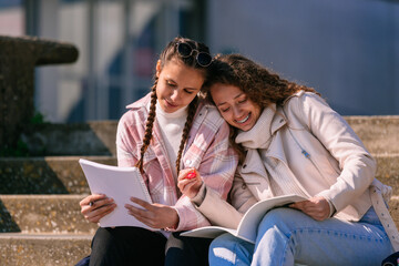 Two young girls sitting on steps, reading books and smiling