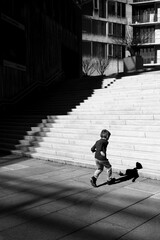 Grayscale shot of a boy running up a set of stairs in an outdoor urban setting.
