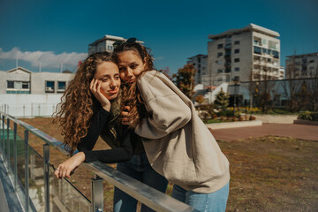 Fototapeta premium An attractive curly haired girl did a big mistake. Her brunette friend is comforting and hugging her. She is stroking her head