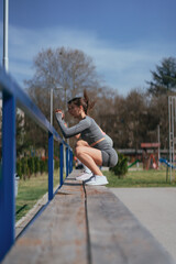 Active sportsgirls exercising legs. Doing jumps on the bench in the park. Side view shot