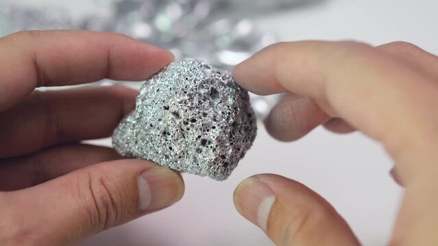 Man's hand holding a lump of silver or platinum or a rare earth mineral on white background	