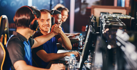 Professional cybersport team. Two happy male gamers shaking hands, celebrating success while participating in eSports tournament