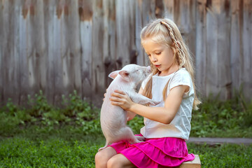 a girl  plays with a pig in the yard of the house. Children take care of pets.