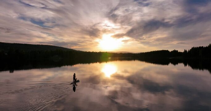 Silhouette of a person kayaking in a lake during sunset