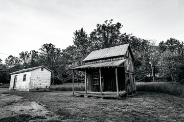Scenic view of old wooden cabins on a grassy hill in grayscale