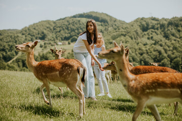 Little girls among reindeer herd on the sunny day