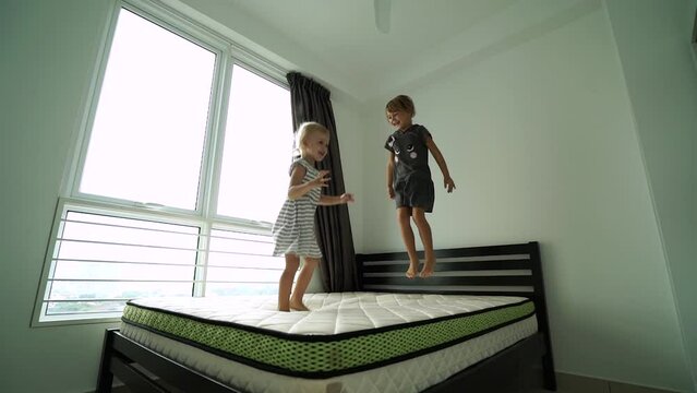 Two happy sisters jumping on mattress bed while have fun after moving into a new home