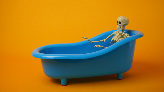 Sitting skeleton in blue bath on a yellow background.