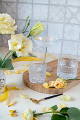 three glasses with a cocktail on a long stem on a wooden tray on the kitchen table, next to yellow flowers in a white vase