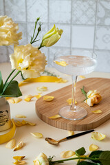 a glass with a cocktail on a long stem on a wooden tray on the kitchen table, next to yellow flowers in a white vase