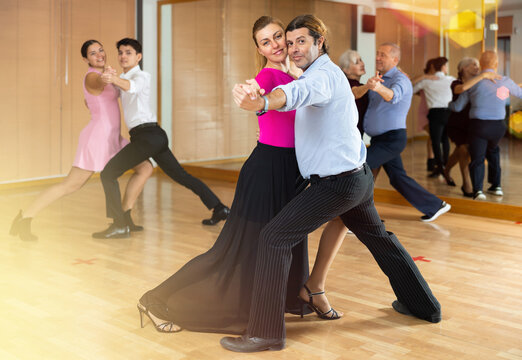 Active middle-aged pair practicing ballroom dance in training hall during dancing-classes. Pairs training ballroom dance
