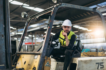 Industrial worker driving a forklift in the factory. Engineer is working and maintaining in the warehouse.