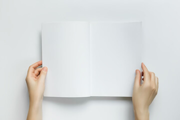 woman holding open book with blank white pages on white table, top view, space fo text