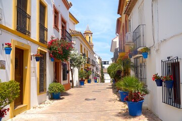 narrow beautiful street in the old town of Estepona with lots of flowers and a view to the church tower of Parroquia Nuestra Señora De Los Remedios, Málaga, Andalusia, Spain