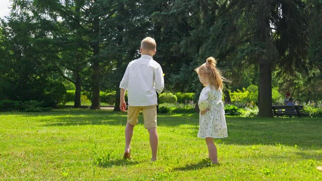 Siblings running and playing with paper plane toy. Happy child playing outdoors. Brother and sister. Family weekend in park. Caucasian kid throwing paper plane and playing together. 4K, UHD