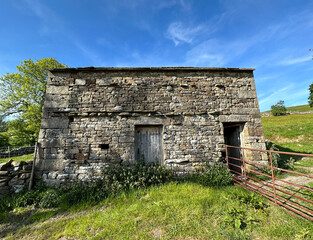 Old stone barn, next to a farmgate, with fields, hills, and a blue sky in, Oughtershaw, Skipton, UK