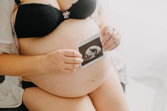 Young pregnant woman with the belly and babys ultrasound paper in hand, pregnancy concept