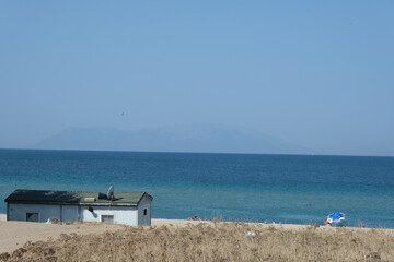 A blue beach with blue sky and a small island in the back in Enez Edirne. There is also a small house in the front