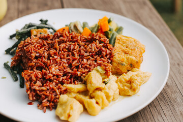 Brown delicious rice with vegetables and egg on a white plate close-up. Asian lunch with beans and tofu close-up