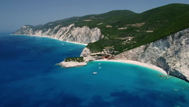 Aerial drone footage with panning motion of  Porto Katsiki in Lefkada, Greece. Sailing boats anchored in shallow turquoise sea waters near the Porto Katsiki beach 