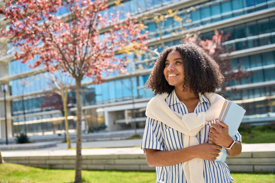 Happy smiling African American girl student standing in university park looking away outdoor dreaming of applying foreign university, study abroad, thinking of admission and scholarship, copy space.