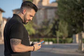 Young man in small town consulting his mobile phone at sunset.