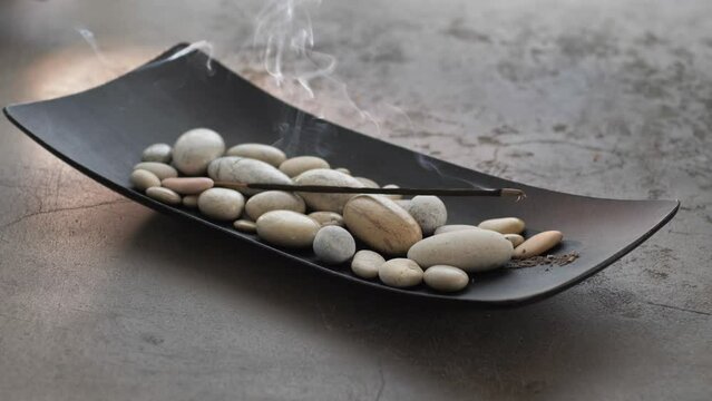 Burning incense aroma stick with smoke, fixed on pebble stones 