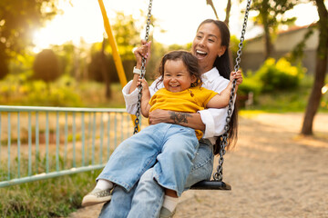 Japanese Mom Sitting With Toddler Infant Daughter Swinging on Playground