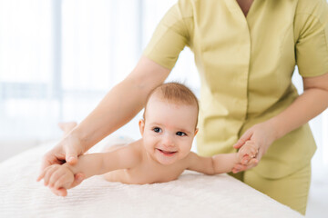 Cropped shot of unrecognizable pediatric masseur with cute baby boy doing exercise simple exercises to make baby bones and muscles stronger. Portrait of laughing newborn infant lying on bed.