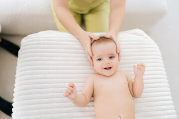 Top view of infant baby boy being manipulated by unrecognizable osteopathic manual therapist or physician. Closeup of female masseuse massage head of small newborn kid. Concept of infant healthcare. - Powered by Adobe