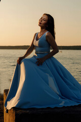 Portrait of a girl in a dress on the riverbank against the sunset sky