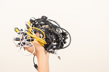 Hand held up with pile of tangled old smart technology wires, used charging cables and cords....