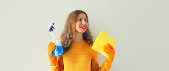 House cleaning concept - housewife or cleaner, happy smiling woman in rubber protective gloves holding dry microfiber rag and detergent spray bottle - obrazy, fototapety, plakaty