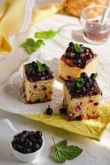 Sliced blackcurrant cake covered with chocolate icing on a square light plate on a light concrete background.