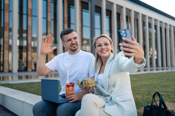 Euphoric delighted young teamworkers taking photos on break while eating healthy food and holding...