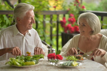 Happy elderly man and woman in casual outfits sitting at kitchen table, having healthy breakfast...