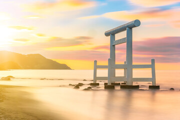 Sunset long exposure photography of a Japanese white wooden torii arch with its pillars in the sea...