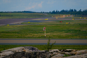  An airport tarmac with a windsock next to the taxiway. Runway markings and lights.