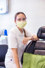 Lifestyle portrait of woman dentist doctor in medical mask and glasses sitting at dental office in...