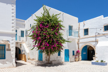 The street of Houmt Souk in Tunisia, white city with blue doors and windows and pink flowers.
