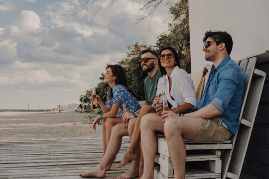 Group of joyful young friends enjoying beer while spending carefree time near the beach house