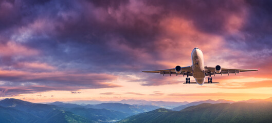 Fototapeta na wymiar Plane is flying in colorful sky at sunset. Landscape with passenger airplane, mountains, purple sky with orange and pink clouds. Aircraft is landing. Business. Aerial view. Transport. Private Jet