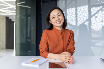 Portrait of young Asian successful business woman, female worker at workplace inside office smiling...