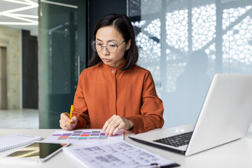 Serious thinking female financier on paper work, Asian concentrated writing data in forms, using laptop at work, reviewing contracts financial reports, accountant at workplace.